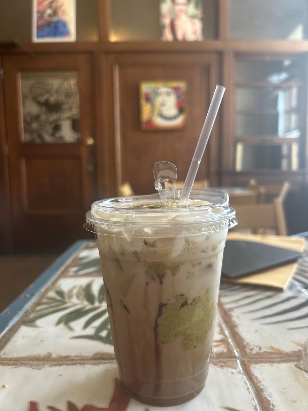 An iced layered drink on a patterned tile table, with framed folk art softly out of focus behind it.
